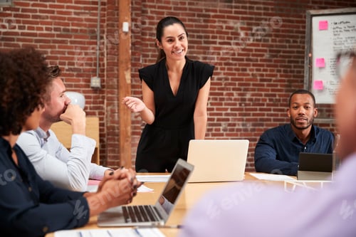 Preview: Young Businesswoman Standing And Leading Office Meeting Around Table