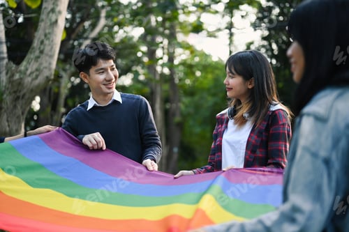 Preview: Image of young people having fun holding LGBT rainbow flag outdoor.