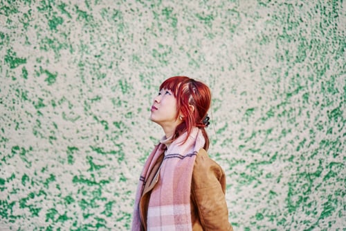 Preview: Red-haired Chinese Woman Looking Up at the Sky on Neutral Background with Copy Space