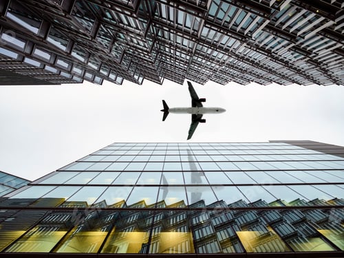 Preview: Low angle view of airplane flying between modern buildings, London City Airport, London, UK