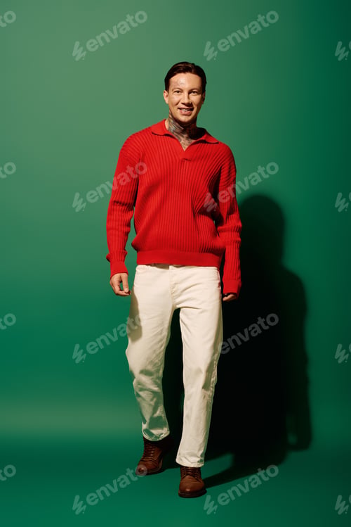 Preview: A young man in a vibrant red sweater and white pants stands against a green backdrop