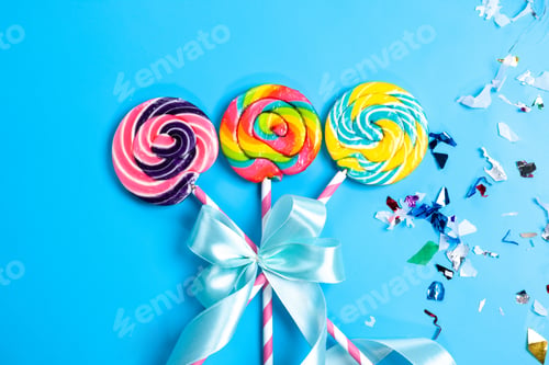Preview: a top view colorful lollipops on the pink-white sticks bowed on the blue background sugar rainbow