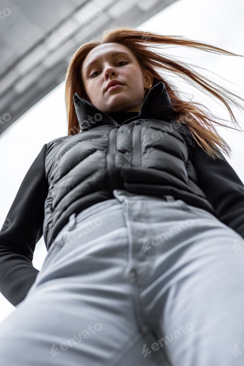 Preview: Bottom view young student woman in black jacket and blue jeans stay outdoors rest look down. People