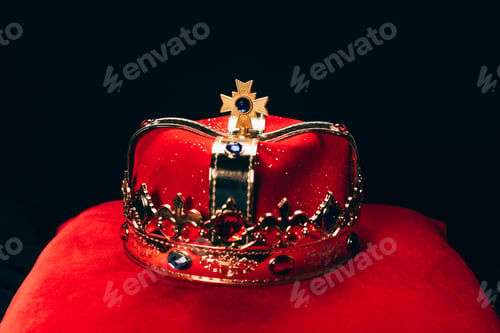 Preview: ancient golden crown with gemstones on red pillow, isolated on black