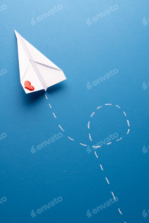 Preview: Vertical of paper plane with red heart and white trail, on blue background with copy space