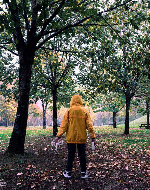 Preview: Back view of a little Caucasian boy in a yellow coat holding a drone and remote control in the park