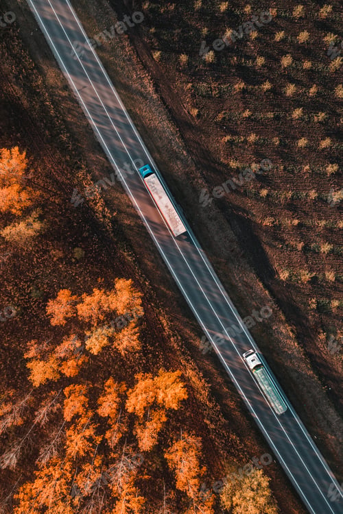 Preview: Aerial shot of two trucks on the road through deciduous forest in fall afternoon, drone pov top down