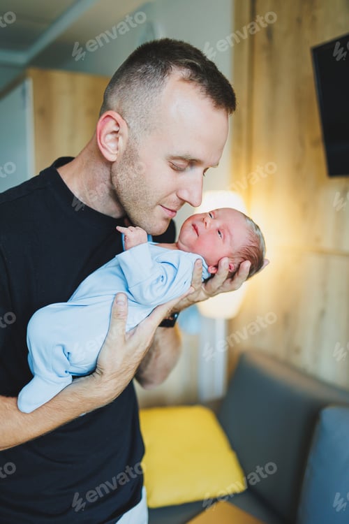 Preview: Happy young dad holding his newborn baby in his arms. Romper on a newborn boy.