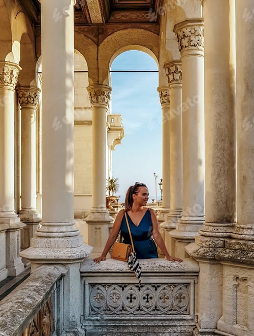 Preview: Portrait of young woman on balcony of a palace with arched colums and pillars with beautiful details
