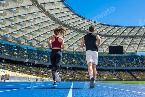 Preview: rear view of male and female joggers running on track at sports stadium