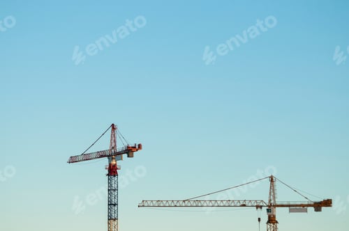 Preview: Cranes towering against a clear blue sky at a construction site.