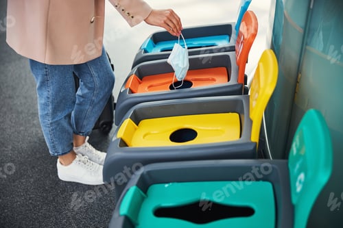 Preview: Female hand throwing medical mask in trash can at airport