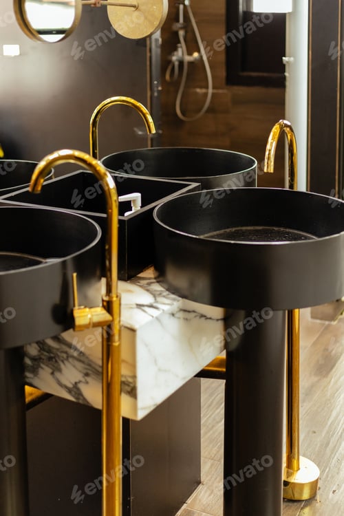 Preview: Multiple black sinks with gold faucets are arranged in a modern bathroom.
