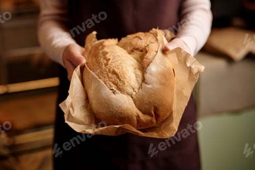 Preview: Close up of young woman carefully holding fresh bread in artisan bakery
