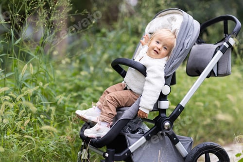 Preview: Adorable baby with blonde hair and smiley face walking outside at fall season in park