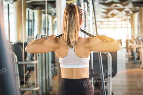 Preview: Back view of sporty woman doing pull ups on cable weight machine in gym.
