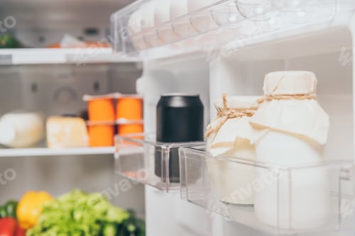 Preview: selective focus of jars with sour cream and black can with soda on fridge door near fresh food on