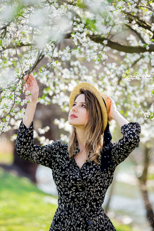 Preview: Young girl in a hat stay near a flowering tree