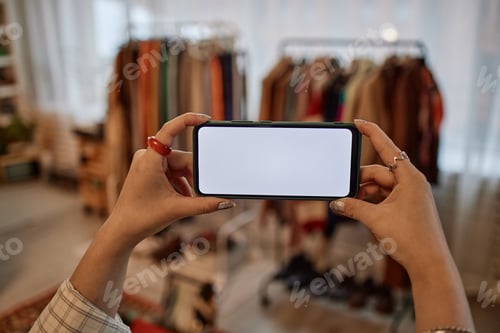 Preview: Young Adult Woman Photographing Second Hand Clothing with Smartphone Indoors