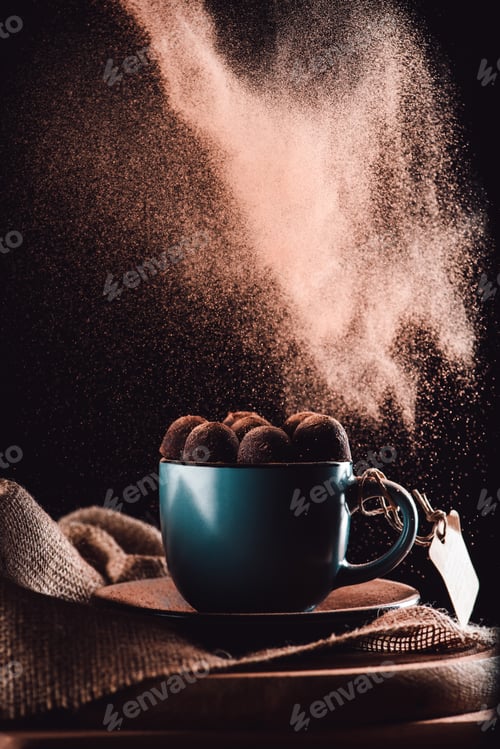 Preview: closeup image of grated chocolate falling on truffles in cup of coffee on sackcloth and cutting