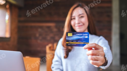 Preview: A woman holding and showing credit cards while using laptop computer for online payment