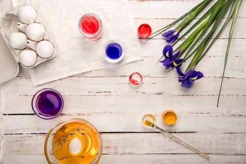 Preview: Top view of chicken eggs in box with paints and iris flowers on wooden table