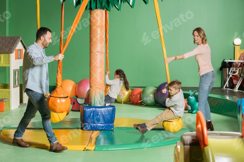 Preview: smiling parents looking at happy kids swinging on swings in indoor play center