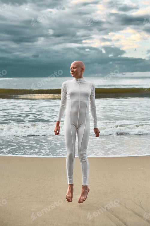 Preview: Candid hairless girl with alopecia in white futuristic suit twirls in jump on sea sandy beach