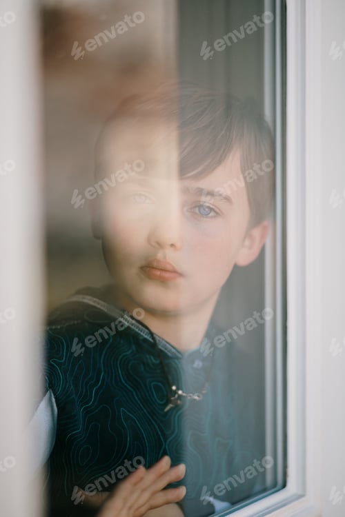 Preview: Young boy looking out of home window door.