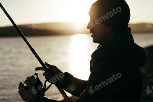 Preview: Young fisherman standing on the shore of lake with fishing rod
