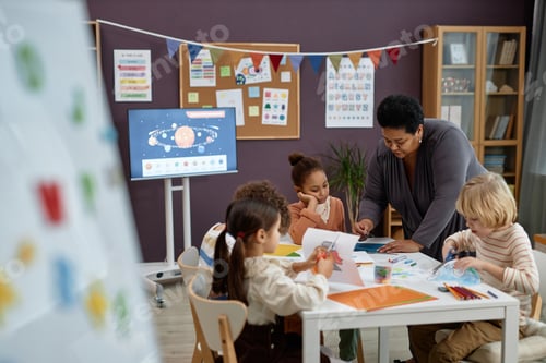 Preview: Black woman helping group of little kids sitting at table in preschool class