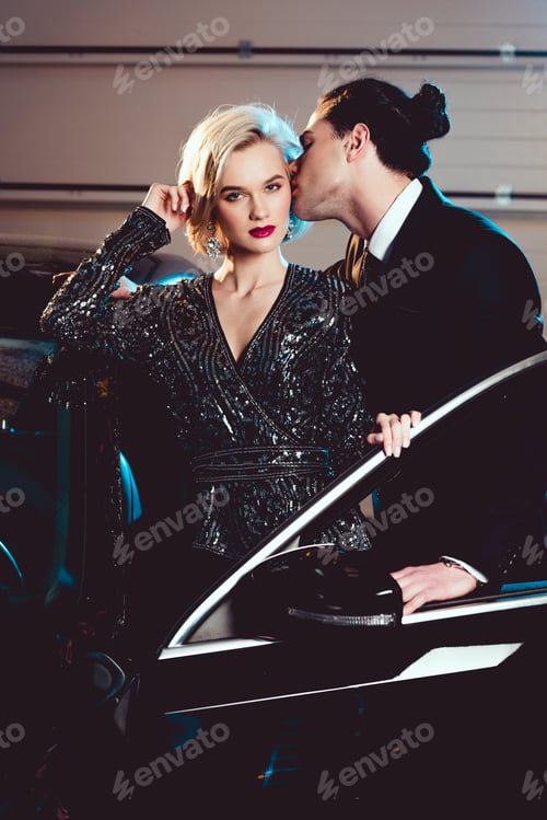 Preview: stylish man kissing beautiful seductive woman near car