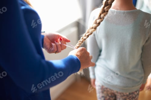 Preview: Cropped view of mother plaiting schoolgirl daughter's hair