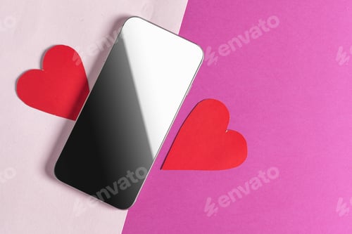 Preview: Smartphone placed between two red paper hearts on a pink and beige surface