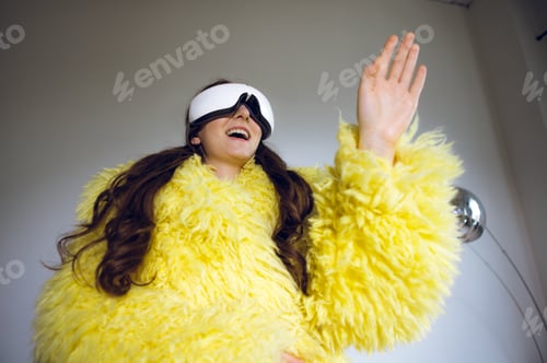 Preview: A young woman in a yellow fluffy jacket and virtual reality glasses