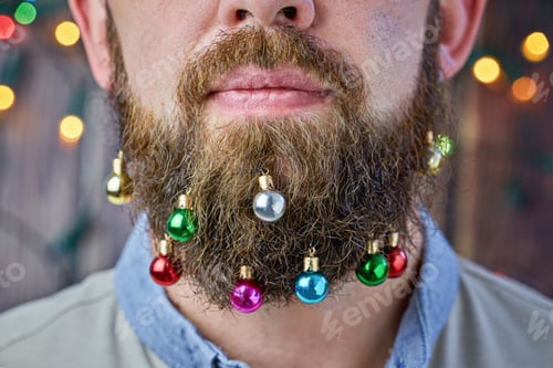 Preview: Close up of hipster man with colorful beard baubles Christmas ball in beard. Trendy Xmas decoration