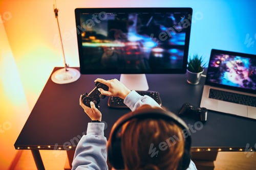 Preview: Teenager girl playing video game at home. Gamer holding gamepads sitting at front of screen