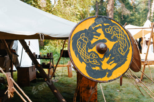 Preview: Medieval military camp, tent and round yellow shield with wolf pattern design outdoors.