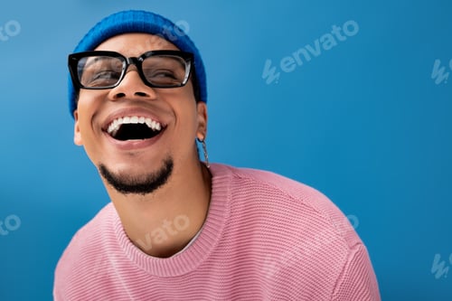 Preview: Young man smiles brightly, showcasing fashion style against a vibrant blue backdrop