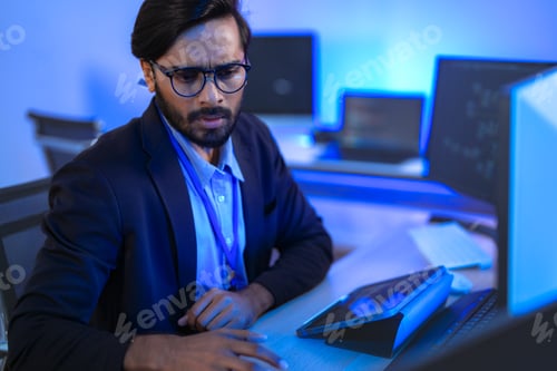 Preview: focused Indian financial analyst or software developer working late in a modern office