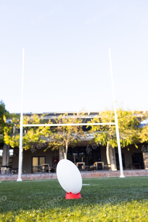 Preview: A rugby ball sits ready for kickoff on a bright field outdoors, copy space