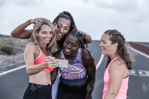 Preview: Happy diverse sportswomen using smartphone together