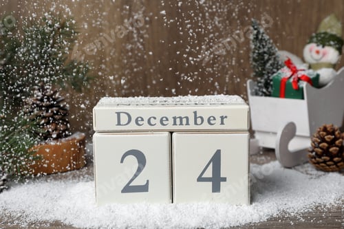 Preview: December 24 - Christmas Eve. Snow falling onto wooden block calendar and festive decor on table