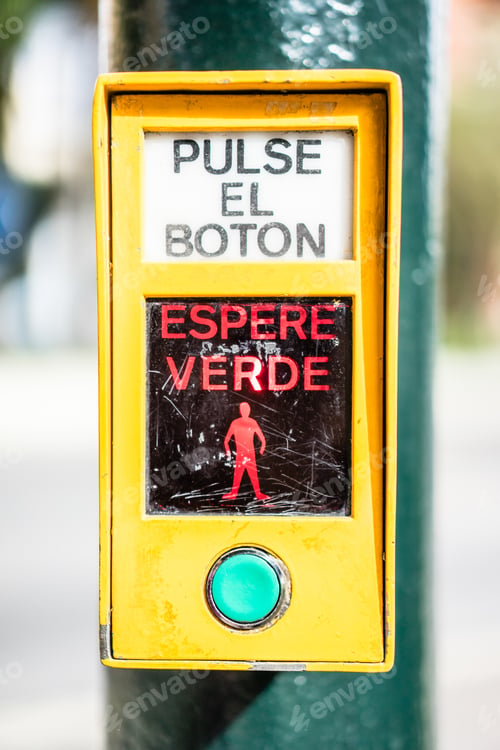 Preview: Vertical closeup shot of a sidewalk crossing button with spanish text