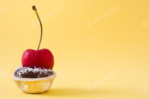Preview: Chocolate tartlet with fresh cherry and grated coconut topping on yellow background