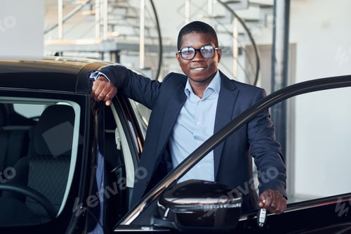 Preview: Holding keys in hands. Young african american businessman in black suit is the autosalon
