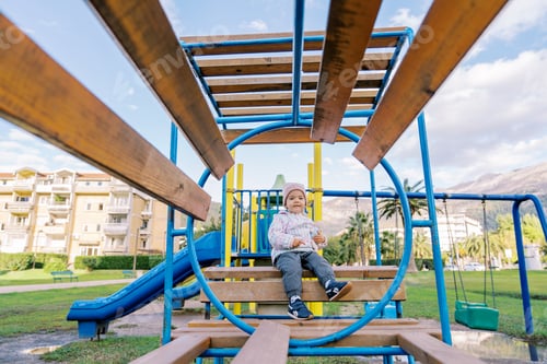 Preview: Little girl sits on a wooden bench with rings on the playground