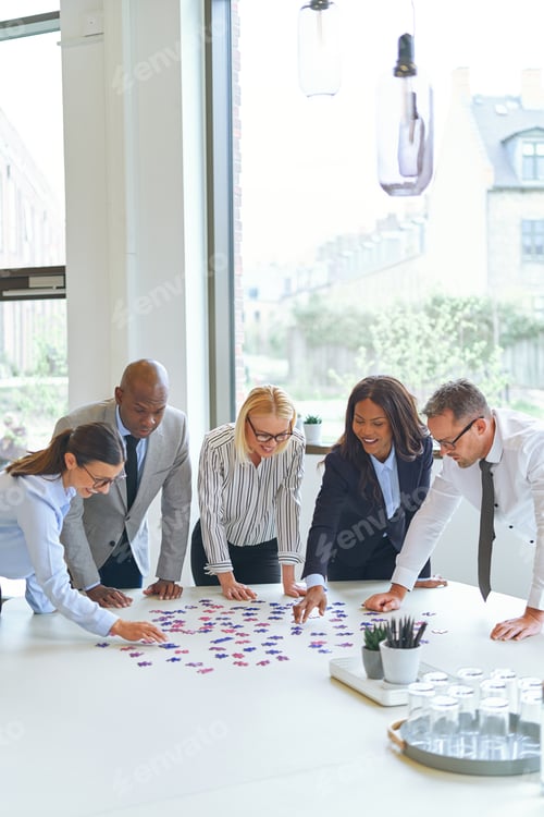 Preview: Smiling businesspeople solving a puzzle on an office table