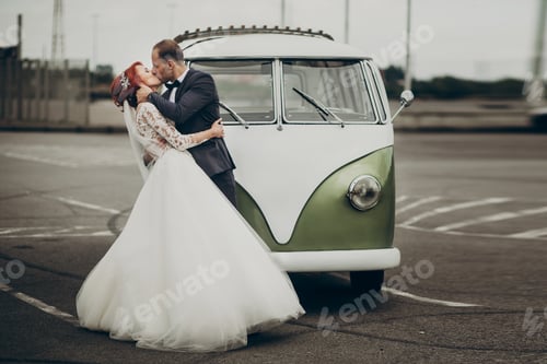 Preview: Stylish bride and groom sensually posing near retro car