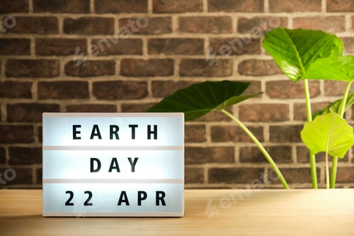 Preview: vertical image with a luminous sign that says earth day april 22 on a brick wall